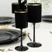 A set of black plastic wine goblets with gold rims displayed on a formal dining table.