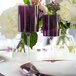 A pair of two-toned purple and clear plastic wine goblets displayed on a table with floral arrangements in the background.