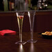 A pair of clear square plastic disposable champagne flutes, one filled with a beverage and a garnish, displayed on a table.