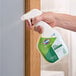A hand holding a spray bottle of Clorox EcoClean glass cleaner being used to clean a glass surface.