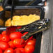 Sabert disposable silver plastic serving tongs picking up a tomato from a tray.