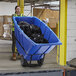 A large blue heavy-duty tilt truck or trash cart with black garbage bags inside, designed for industrial use.