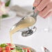 A stainless steel gravy boat being used to pour dressing onto a salad.