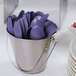 A metal bucket filled with purple heavy weight plastic spoons.