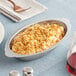 A stainless steel oval au gratin dish filled with a baked, breadcrumb-topped casserole.