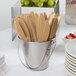 A small metal bucket filled with gold-colored plastic knives on a table.