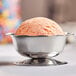 A stainless steel paneled sherbet dish holding a scoop of orange sherbet.