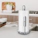 A brushed stainless steel tension arm paper towel holder with a roll of paper towels on a kitchen counter.