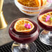 A glass of dark red cocktail garnished with a dried orange slice and a small pink flower.