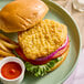 A plant-based vegan crispy breaded chicken fillet sandwich with lettuce, tomato, and red onion on a bun, served with fries and ketchup.