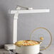 A white multi-position infrared heat lamp positioned above a pot of food.