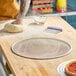 A round, heavy duty expanded aluminum pizza screen on a wooden countertop.