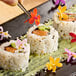A plate of sushi rolls garnished with colorful Fresh Origins Micro Orchid edible flowers.