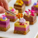 A selection of colorful, layered dessert squares being decorated with Fresh Origins micro edible flowers using tweezers.