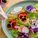 A plate of assorted Fresh Origins pansy edible flowers being arranged with tweezers.