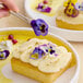 A rectangular dessert topped with piped cream and decorated with Fresh Origins viola edible flowers.