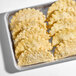 A tray of frozen chicken and cheese empanadas with a crimped edge, arranged in rows.