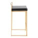 A modern counter height stool with a gold steel frame, low back, and black faux leather seat.