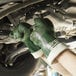 A pair of green nitrile work gloves with white cuffs being worn while working on a vehicle.