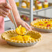 A person spooning peach filling into a pie crust with another filled pie in the background.