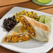 A chicken fajita burrito cut in half, served with black beans, corn, and lime wedges on a white plate.