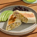 A plate with a pork carnitas burrito cut in half, served with sliced avocado and black beans.