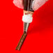 A metal piping tip being used to pipe chocolate icing onto a red surface.