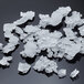 A collection of irregularly shaped, translucent flake ice pieces scattered on a dark surface.
