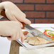 A person using an American Metalcraft stainless steel steak knife with a hardwood handle to cut a piece of meat on a plate.