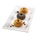 A rectangular white plate displaying three ridged, donut-shaped desserts, two golden and one dark, with coffee beans scattered around them.