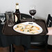 A brown rectangular non-skid serving tray holding a plate of appetizers, a glass of wine, a beer bottle, and an empty glass.