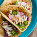 A plate of tacos topped with sliced jalapeños, radishes, cilantro, and drizzled with Mexican crema.