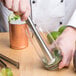 A stainless steel muddler with a tenderizer head being used to crush ingredients in a glass.