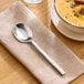 A stainless steel bouillon spoon with a polished finish resting on a beige napkin.