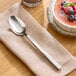 A stainless steel dessert spoon with a modern, squared handle resting on a beige napkin.