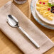 A stainless steel teaspoon with a modern, forged design resting on a beige napkin.