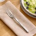 A stainless steel salad fork with a textured handle resting on a beige napkin.