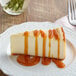 A slice of cheesecake drizzled with caramel sauce on a white plate.