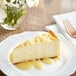 A slice of cheesecake drizzled with white chocolate sauce on a white plate.