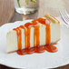 A slice of cheesecake topped with orange pumpkin pie flavored sauce on a white plate.