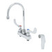 A white T&S deck-mount faucet with silver wrist action handles and a gooseneck spout over a white background.