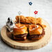 A set of two mini burgers and two fried chicken tenders on a wooden serving board, each burger secured with a red, white, or blue star-topped bamboo pick.