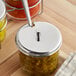 A stainless steel lid with a knob and spoon slot designed for a 7 oz. glass condiment jar.