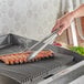 A pair of 16-inch extra heavy-duty stainless steel utility tongs being used to handle ribs on a grill.