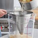 A stainless steel conical strainer being used to strain liquid from a pot into a clear plastic container.