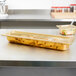 A Vollrath amber high heat plastic food pan with food in it on a counter.