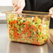 A person cutting carrots into a Vollrath plastic food pan.