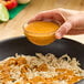 A hand holding a small glass bowl of orange chipotle wine sauce above shredded chicken in a pan.