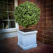 An artificial potted boxwood ball topiary in a square planter placed on a brick patio.