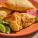 A plate of Brisas chicken flour shell empanadas, with one empanada cut open to show the chicken filling, garnished with lime wedges and herbs.